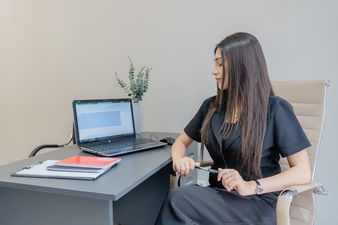 Woman in black dress working at desk with laptop.