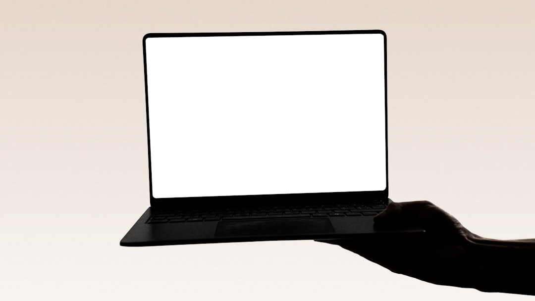 A hand holds a laptop with a blank screen